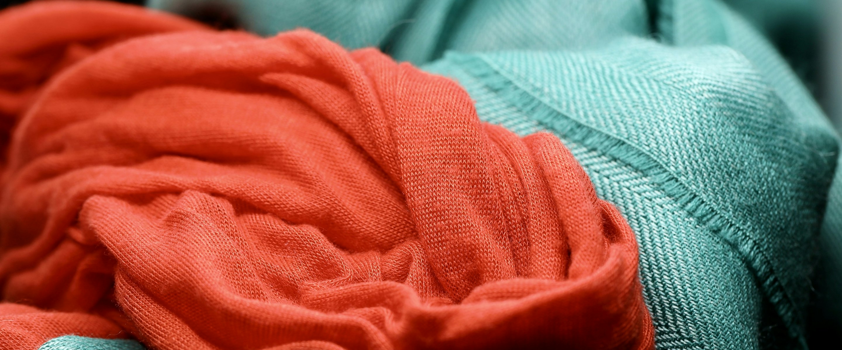A coral jersey knit lying across a teal herringbone fabric