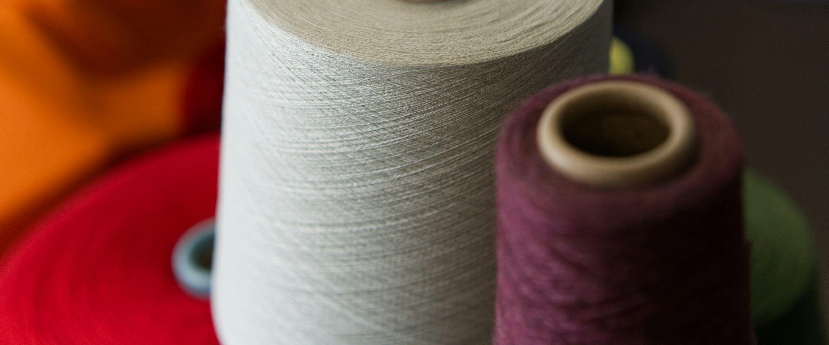 Cones of yarn racked side by side in natural white, wine, orange and red