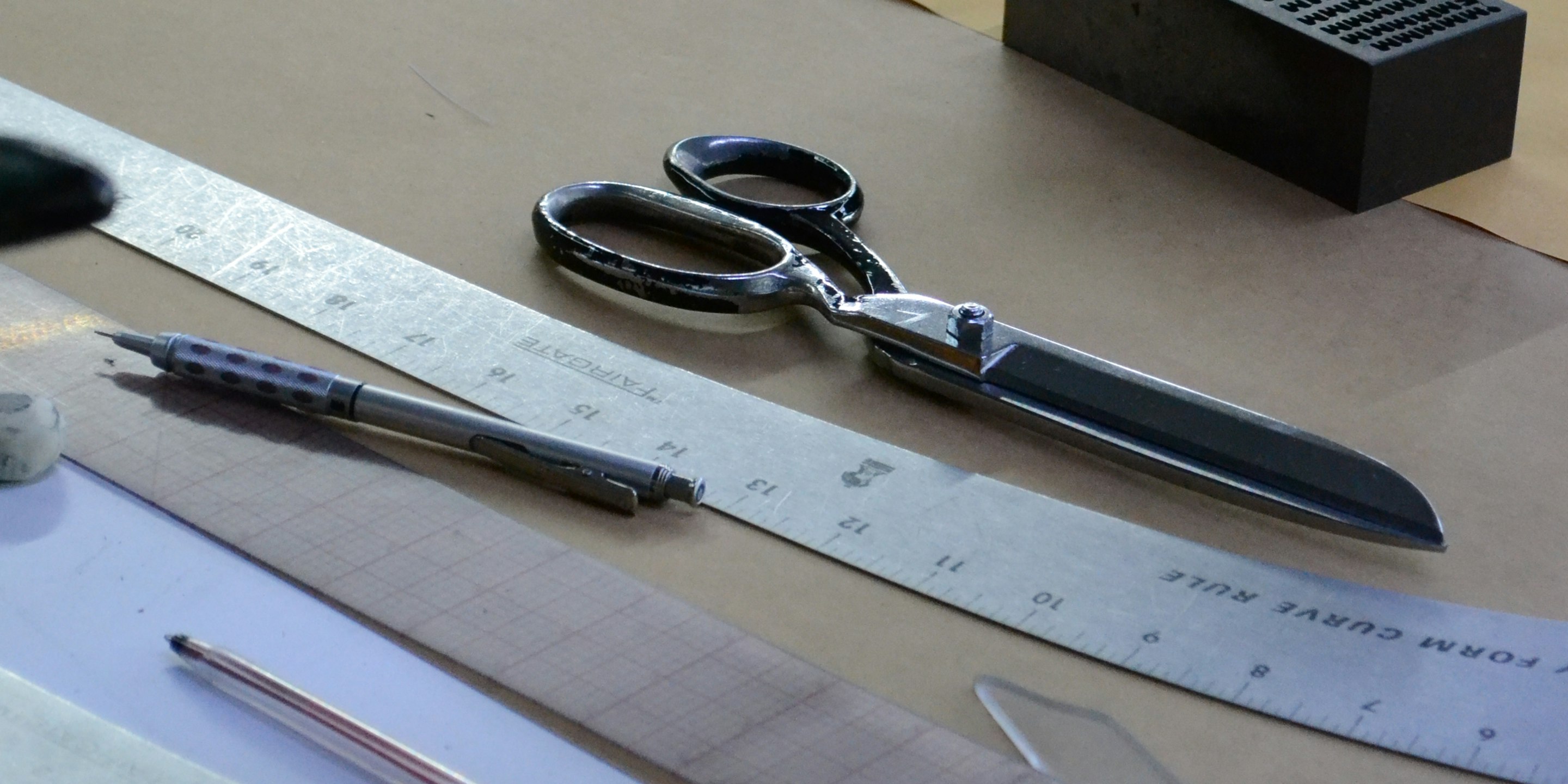 Pattern-cutting tools — scissors, curve ruler, pencil — laid out on marked pattern paper
