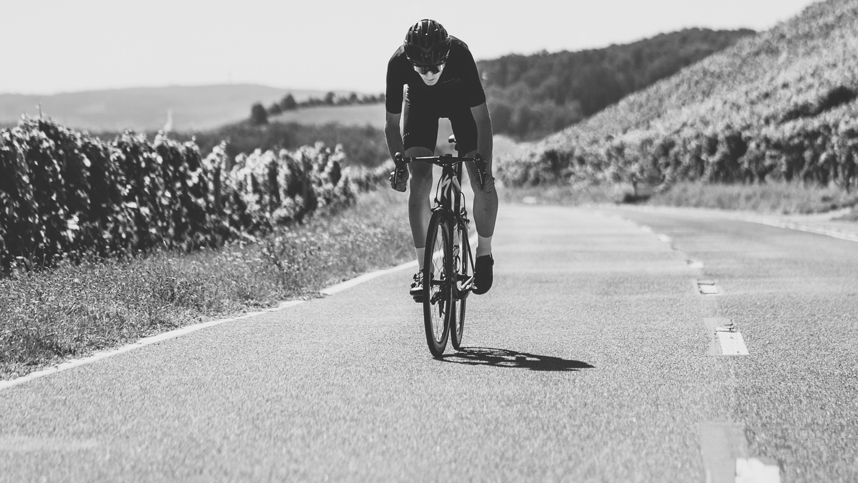 Road cyclist riding in a forward-leaning race posture on a paved road