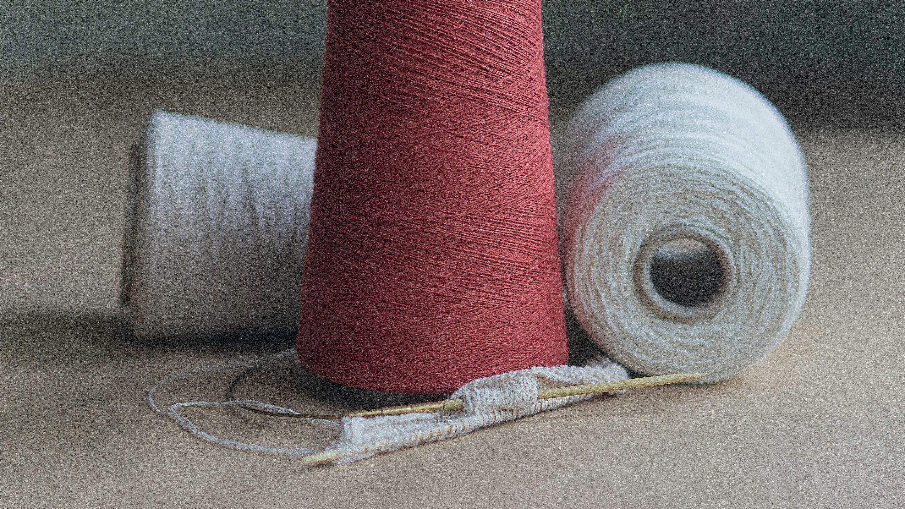 Three cones of thread beside a hand-knitting project in progress