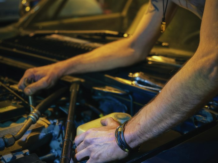 Mechanic in a gray twill mechanic shirt with a name patch and shop logo