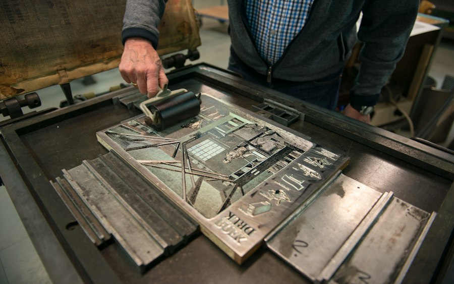 Print shop operator pulling a screen print onto a blank tan canvas work shirt