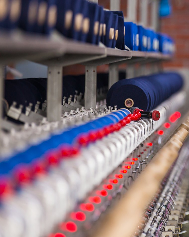 Cutting room worker smoothing stacked twill fabric on a long cutting table