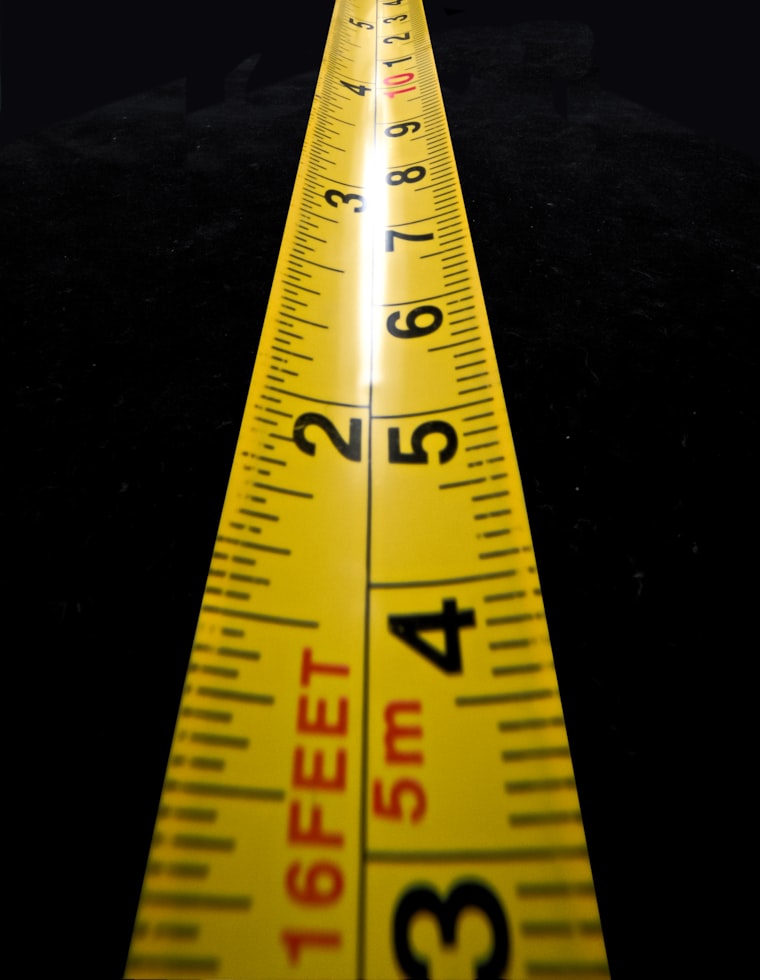 A tailor's tape measuring a hockey pant shell worn over a player's own padded pants, waist measurement taken in the dressed state