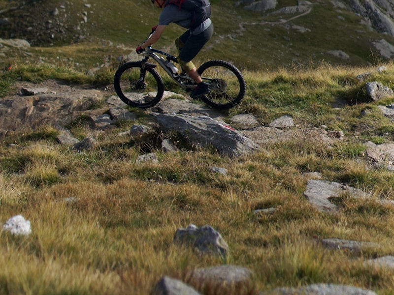 Mountain biker rolling a bike over a rock on a technical alpine singletrack trail